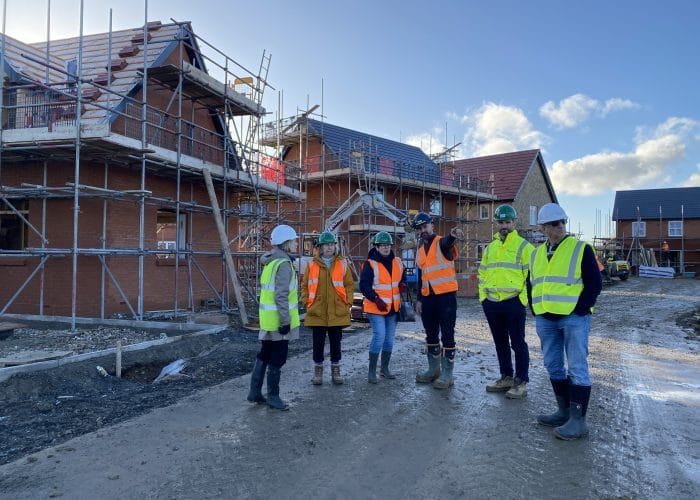 Houses under construction in background with members of the tour discussing the site.